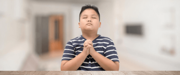 Young boy with hands in prayer position with eyes closed
