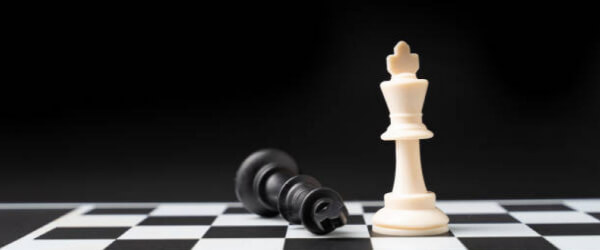 White king chess piece standing next to fallen black king chess peice on black and white chess board