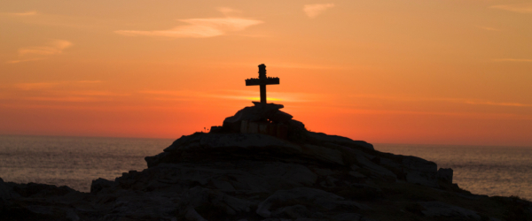 Cross in the distance on top of a hill with the sun setting behind it